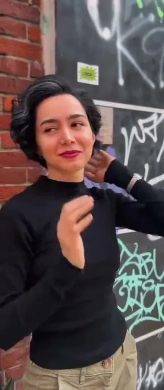 Kort, donker kapsel met golven, buiten tegen een muur met graffiti