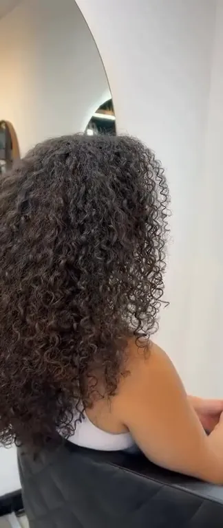 Lang, gedefinieerd krullend haar van achteren, voor een ronde spiegel in de salon